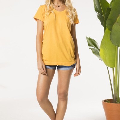 Mulher com t-shirt amarela, calções de ganga e sandálias pretas ao lado de planta em vaso de barro