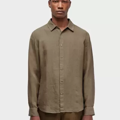 Homem com camisa castanha clara e calças castanhas em fundo cinza.