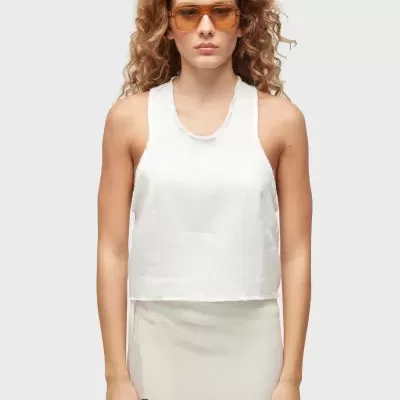 Mulher com óculos de sol, camisola branca de alças e saia bege com padrão negro