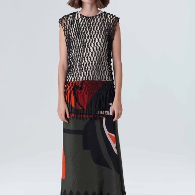 Mulher com saia longa estampada, blusa de malha preta aberta e óculos de sol brancos