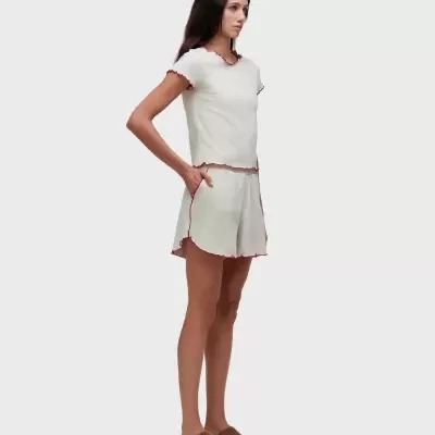 Conjunto feminino branco com t-shirt e calções com bainhas vermelhas e sapatos castanhos.