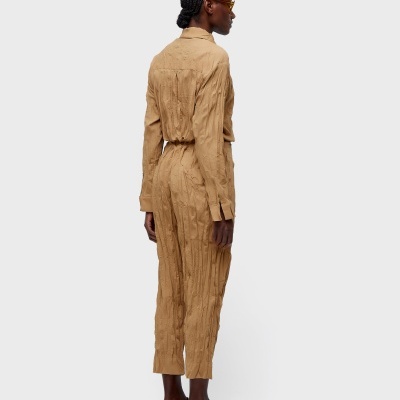 Macacão castanho enrugado com cinto e sapatos claros em fundo branco