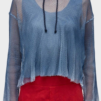 Blusa azul de malha larga com capuz e cordões pretos sobre top azul e calças vermelhas