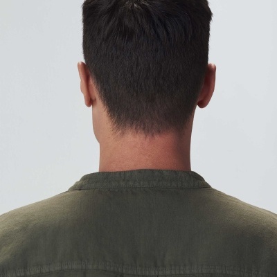 Homem visto de costas com camisa verde-oliva em fundo cinza claro