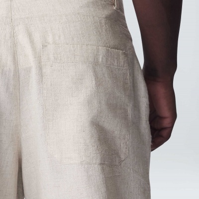 Detalhe das calças de linho bege claro com bolso traseiro e parte de uma camisa branca