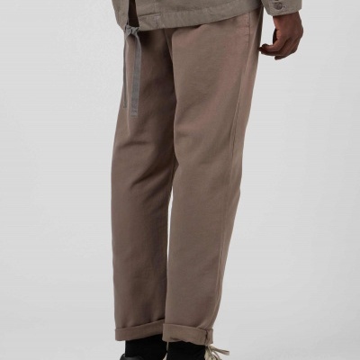 Pessoa vestindo calças castanhas, meias pretas e ténis bege em fundo cinzento