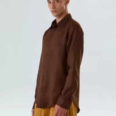 Homem com camisa castanha de manga comprida e calças amarelo mostarda