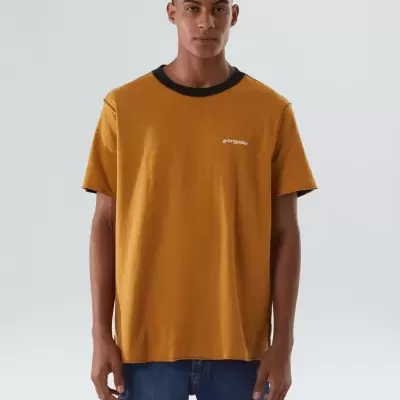 Homem a usar t-shirt mostarda com gola preta e calças de ganga