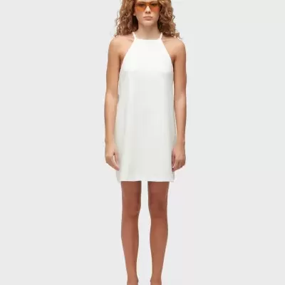 Vestido curto branco sem mangas com decote halter em fundo cinza.