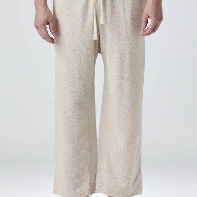 Calças compridas bege claro com cordão ao centro, usadas com chinelos pretos.