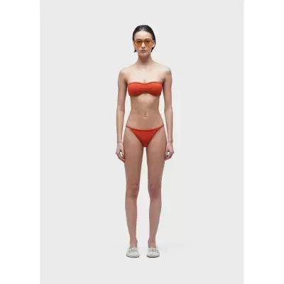 Mulher com fato de banho vermelho, óculos de sol laranja e sapatos brancos.