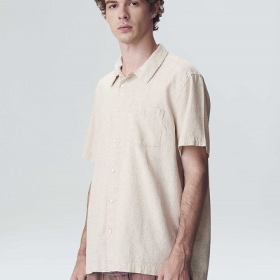 Homem com camisa bege de manga curta e calças xadrez castanhas e vermelhas