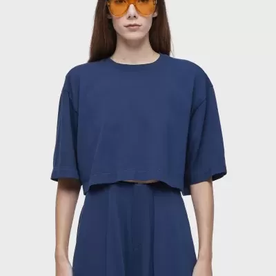 Mulher com óculos de sol laranja e conjunto azul escuro sobre fundo branco.