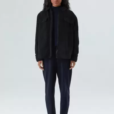 Mulher com casaco preto fofo e calças azul-escuras em fundo branco.