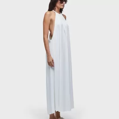 Vestido longo branco com decote halter usado por mulher com óculos e sapatilhas em fundo cinza claro