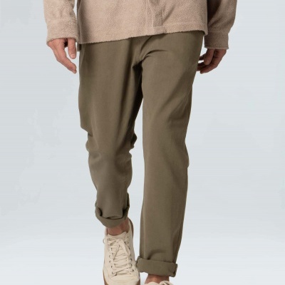 Calças bege-oliva com bainha virada usadas com camisa rosa claro e ténis brancos.