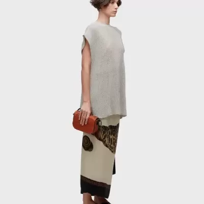 Mulher com camisola cinza de malha e saia comprida estampada, sandálias pretas e carteira laranja