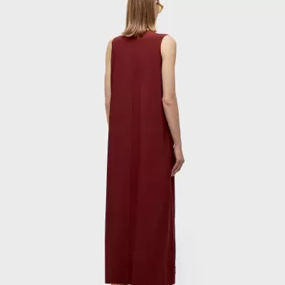 Modelo de costas a usar vestido comprido castanho-avermelhado sem mangas.