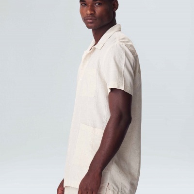 Homem com camisa, calças e boné bege claro em fundo cinza