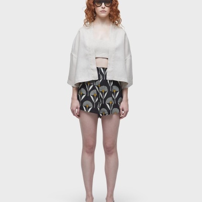 Mulher com camisa branca, top branco, calções estampados e óculos escuros.