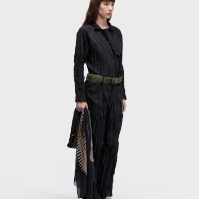 Mulher de macacão preto com cinto verde segurando lenço preto com padrão de penas.
