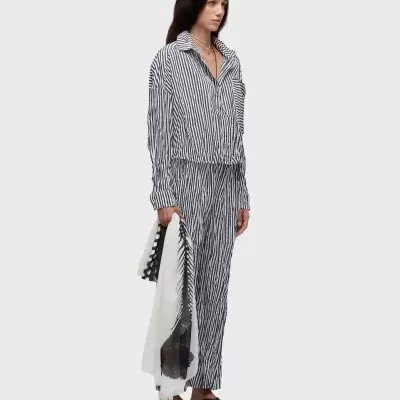 Mulher com camisa e calças riscas pretas e brancas, sandálias pretas, colares e lenço na mão.