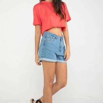 Mulher com t-shirt coral, calções de ganga e sandálias pretas