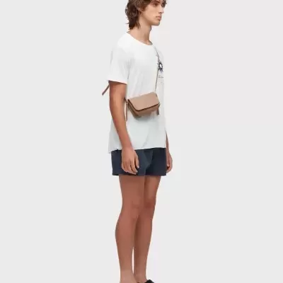 Modelo com t-shirt branca, calções curtos azuis, sapatilhas pretas e bolsa castanha ao peito.