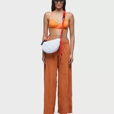 Mulher vestindo top e calças laranja, sandálias brancas e vermelhas, óculos escuros, bolsa branca com alça vermelha.