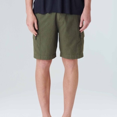 Calções verdes-oliva, camiseta preta e sapatos bege, fundo claro neutro.