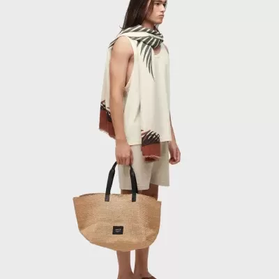 Homem a usar roupa clara e lenço estampado segurando bolsa de palha com alças pretas