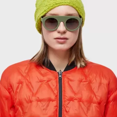 Mulher com gorro verde limão, óculos de sol verdes e casaco vermelho acolchoado