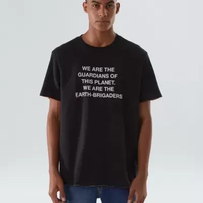 Homem com t-shirt preta com texto branco e calças de ganga azuis