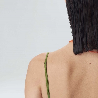 Pessoa de costas com cabelo castanho liso e top verde de alças finas