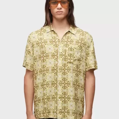 Modelo masculino com camisa de padrão floral amarelo e branco e óculos de sol âmbar