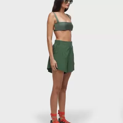 Mulher com top e saia verdes, ténis cinza com atacadores vermelhos e óculos verdes