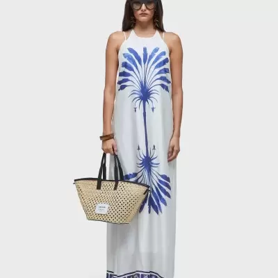 Mulher com vestido maxi branco com estampa azul e mala tote em palha bege