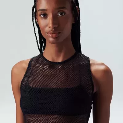 Top feminino preto de malha transparente sobre top opaco numa modelo com fundo neutro