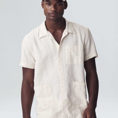 Homem com camisa bege de manga curta, calças e boné bege, fundo branco