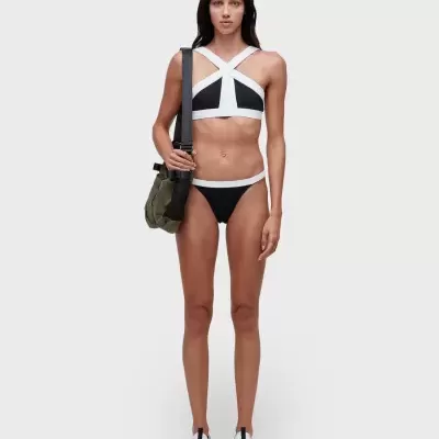 Mulher com biquíni preto e branco, sapatos desportivos brancos e mochila verde-oliva