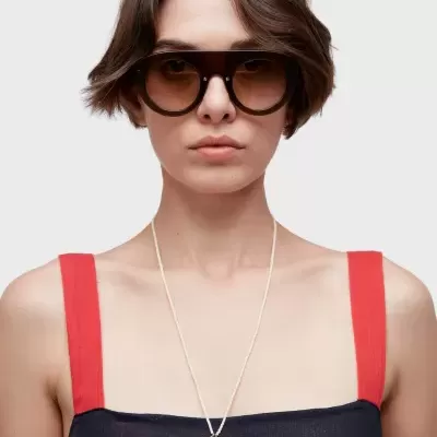 Mulher com óculos de sol, vestido azul com alças vermelhas e colar com pendentes metálicos