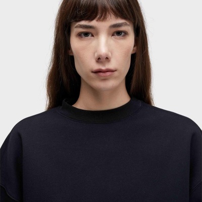 Pessoa com cabelo castanho e franja usando sweat preta com gola redonda