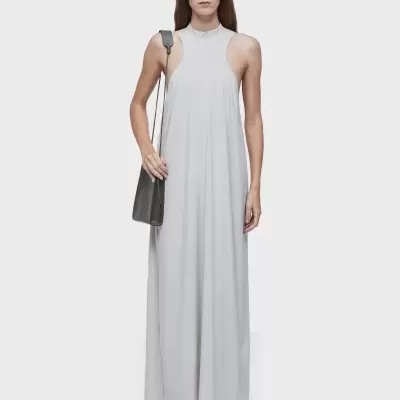 Mulher com vestido cinza claro e mala cinza escura, óculos escuros e sandálias.