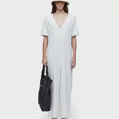 Mulher com vestido branco longo e chapéu branco segurando bolsa preta