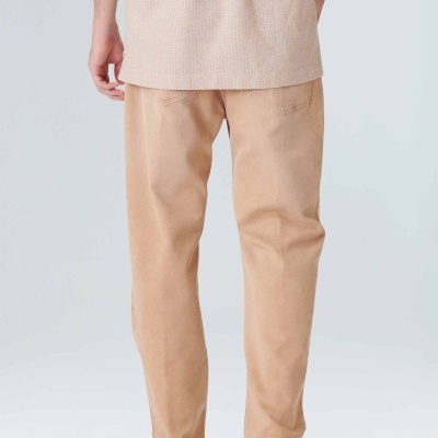 Calças bege vistas de costas usadas por pessoa com sapatos bege e camisa bege clara.