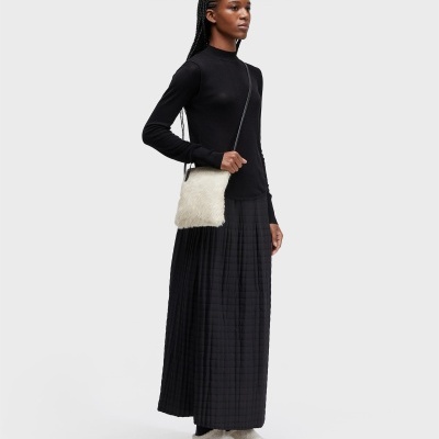 Mulher com blusa preta, saia preta xadrez, ténis brancos e bolsa branca peluda