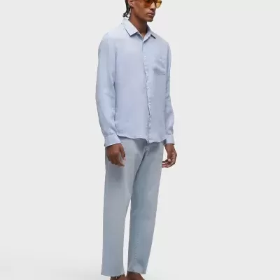 Homem com roupa azul clara e sandálias castanhas em fundo cinza claro