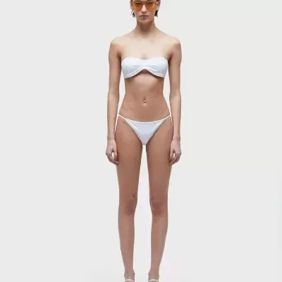 mulher com biquíni branco minimalista, sandálias brancas e óculos de sol de lentes âmbar