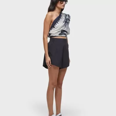 Mulher com top estampado azul e branco, calções pretos, sandálias brancas e óculos de sol pretos