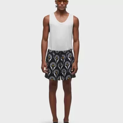 Homem com camisola branca de alça e calça short floral preta com padrão cinza, branco e amarelo.